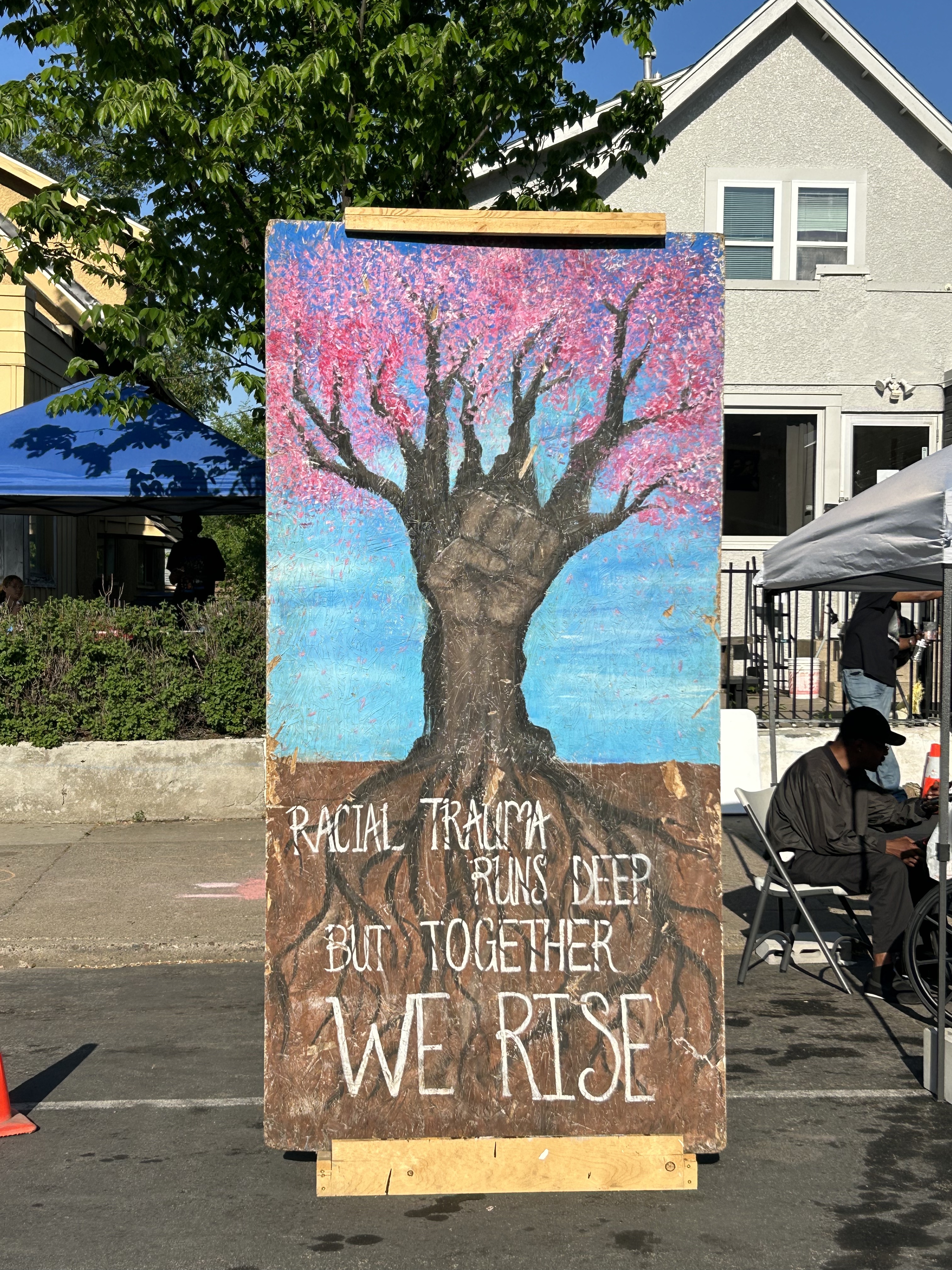 Art depicting a hardwood tree and a fist intertwined. It reads: "Racial trauma runs deep, but together we rise"