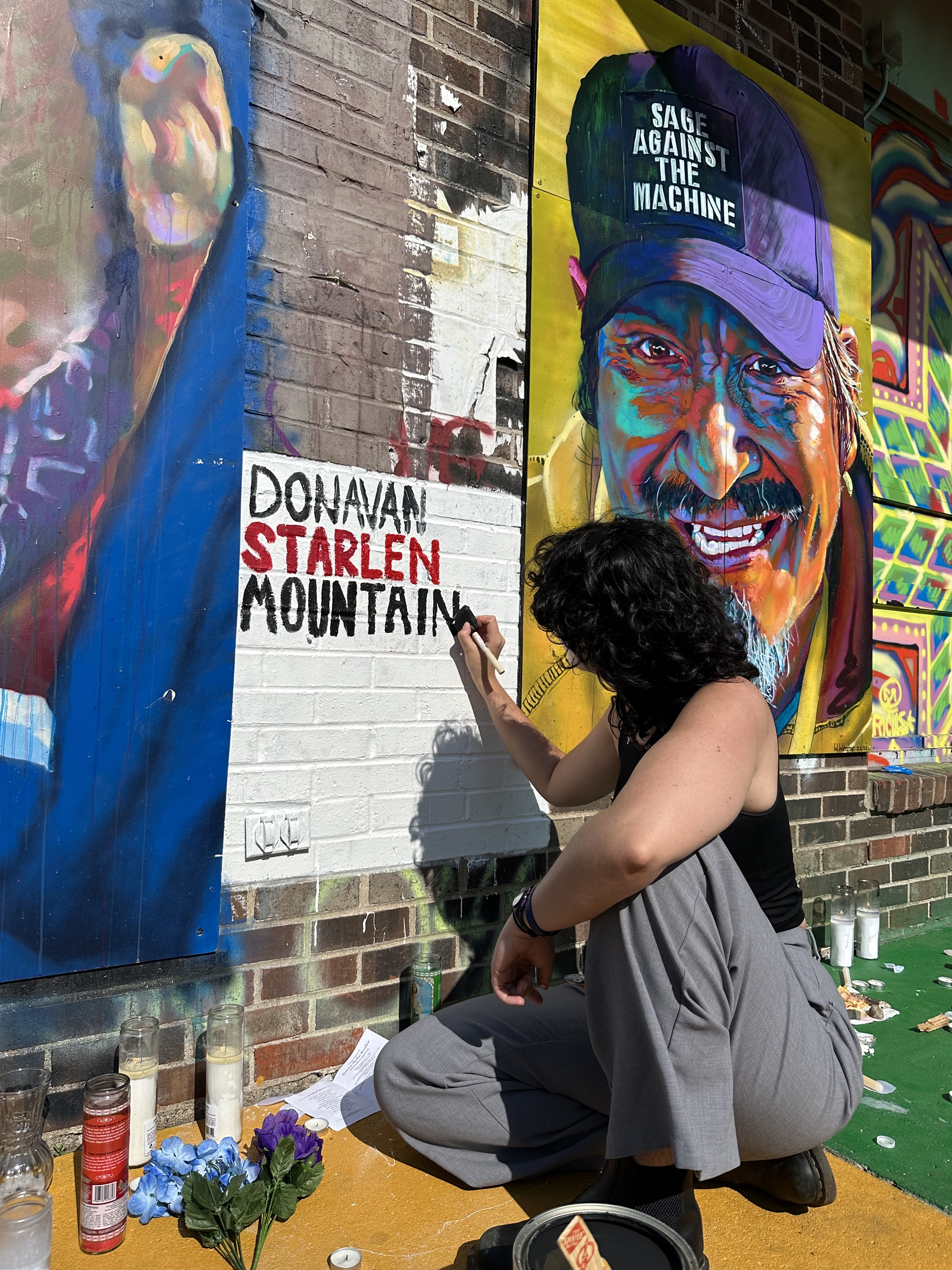 woman crouches, touching up a mural in recognition of Donavan Starlen Mountain