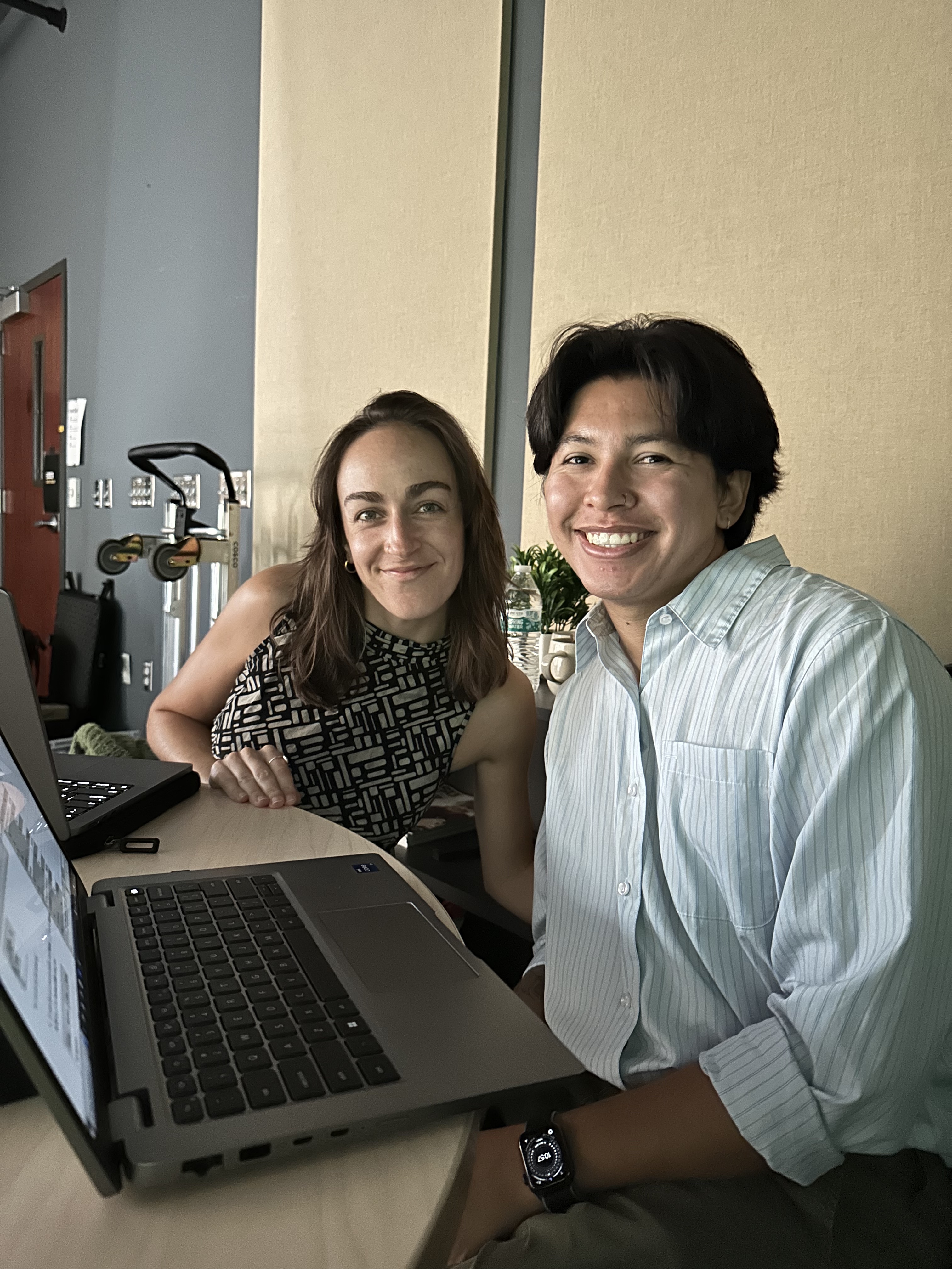 A woman and man sit, smiling, behind a computer.