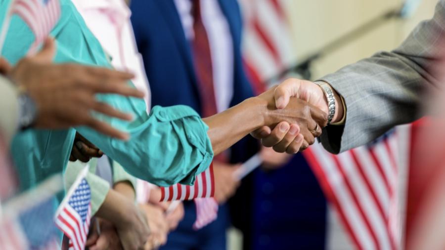 two individuals shaking hands, American flag in background