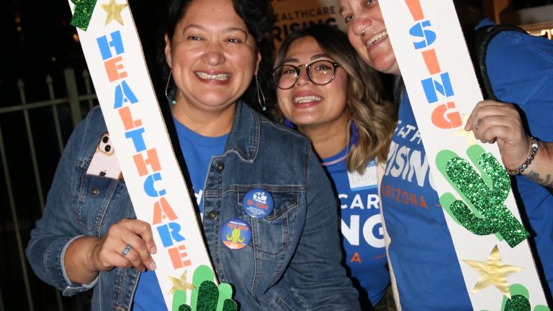 Image of three individuals posing with a Healthcare Rising Arizona sign during their campaign to pass Prop 209.