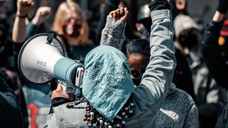 Protest image, fists raised. Person speaking with megaphone.