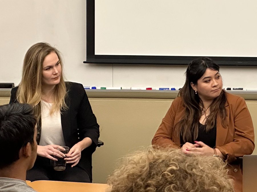 Two women sit at the front of the classroom, looking to the right.
