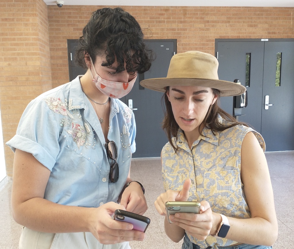 Two women discuss something, looking at their phones.
