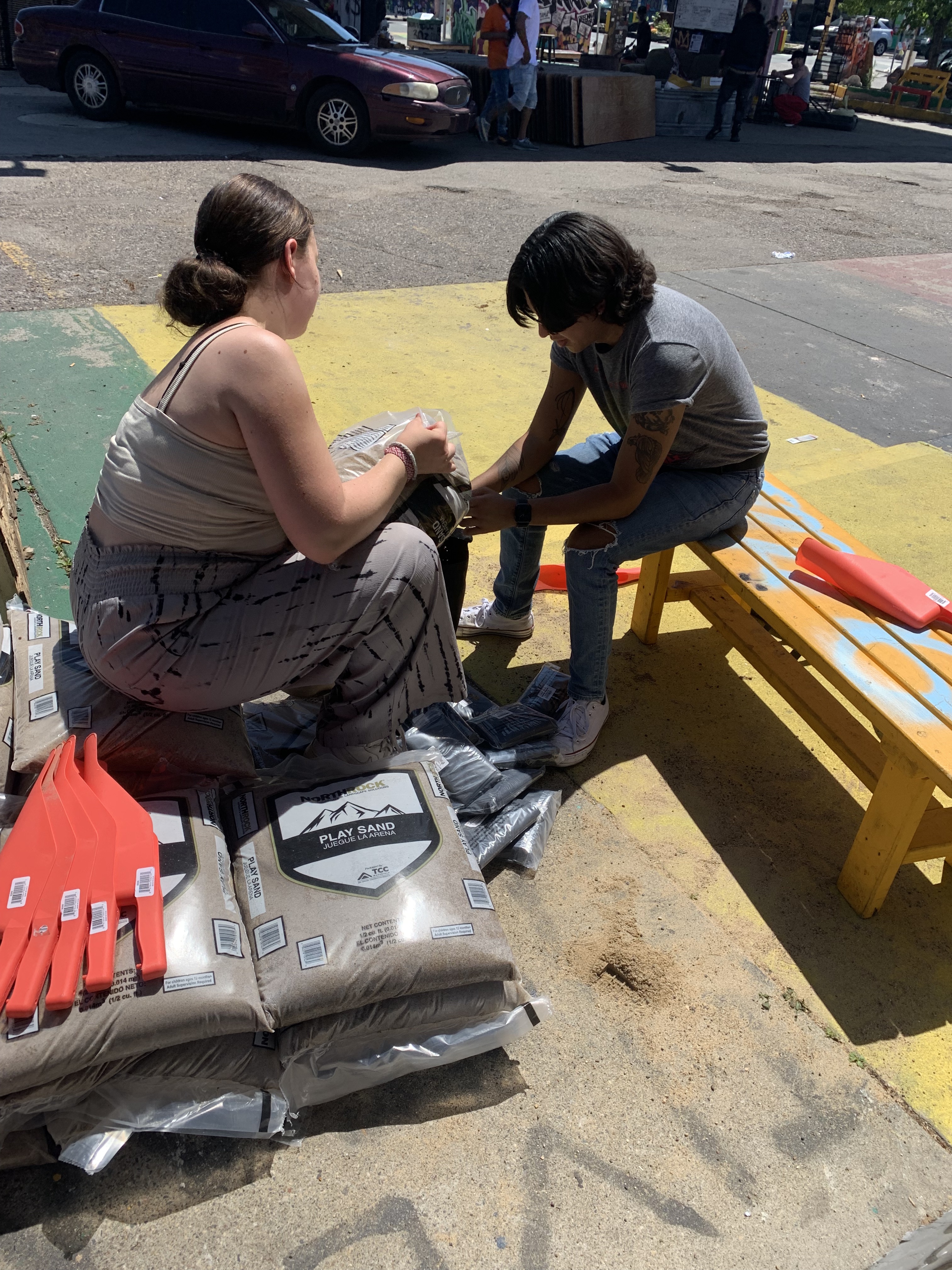 two people sit, filling sandbags.