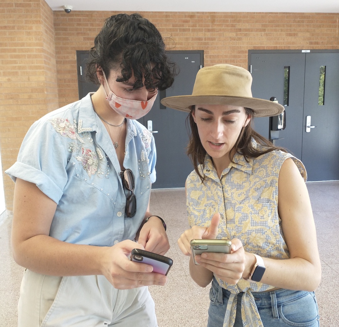Two women discuss something, looking at their phones.