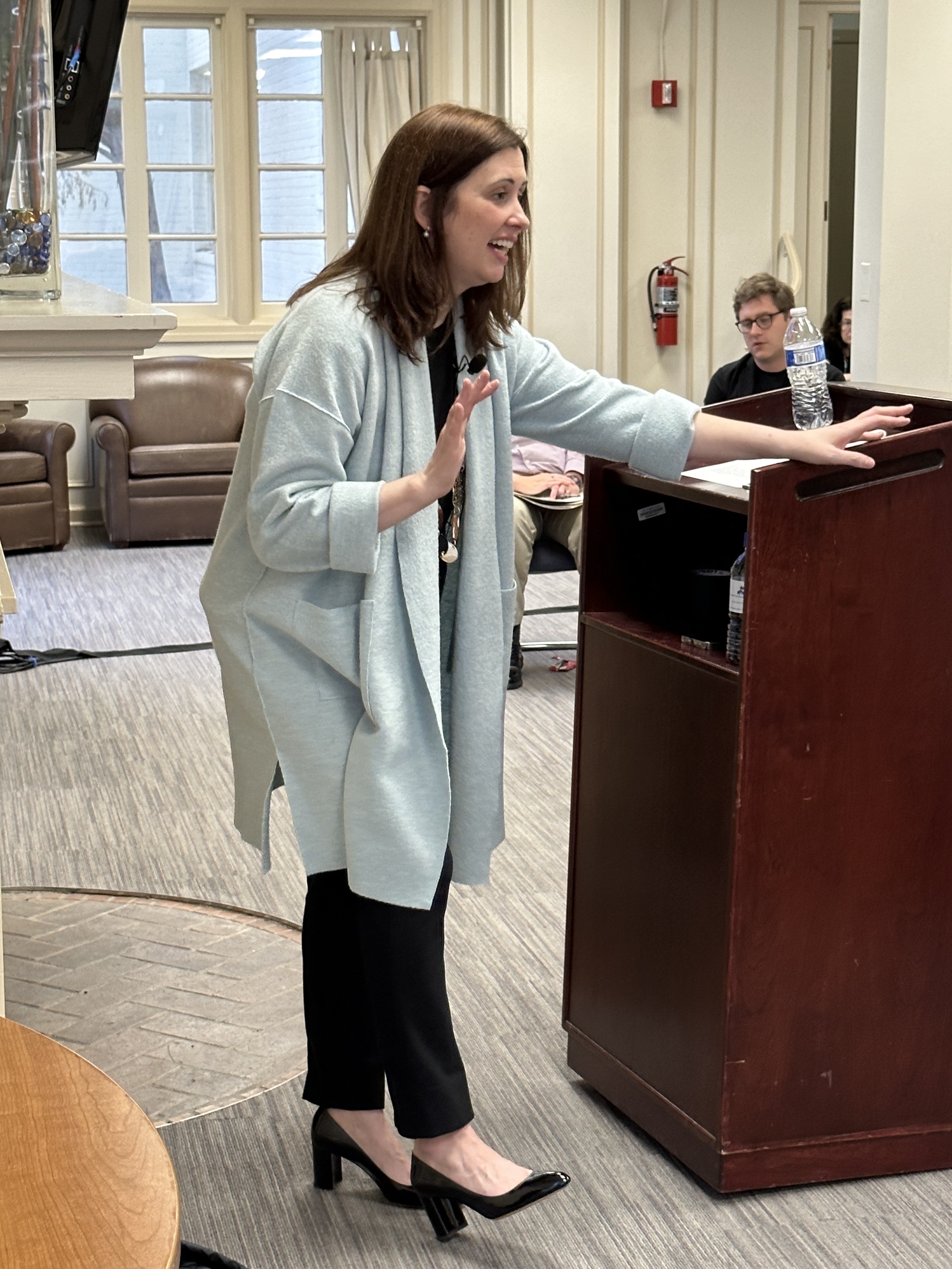 Woman gesturing, leaning against a lecturn.