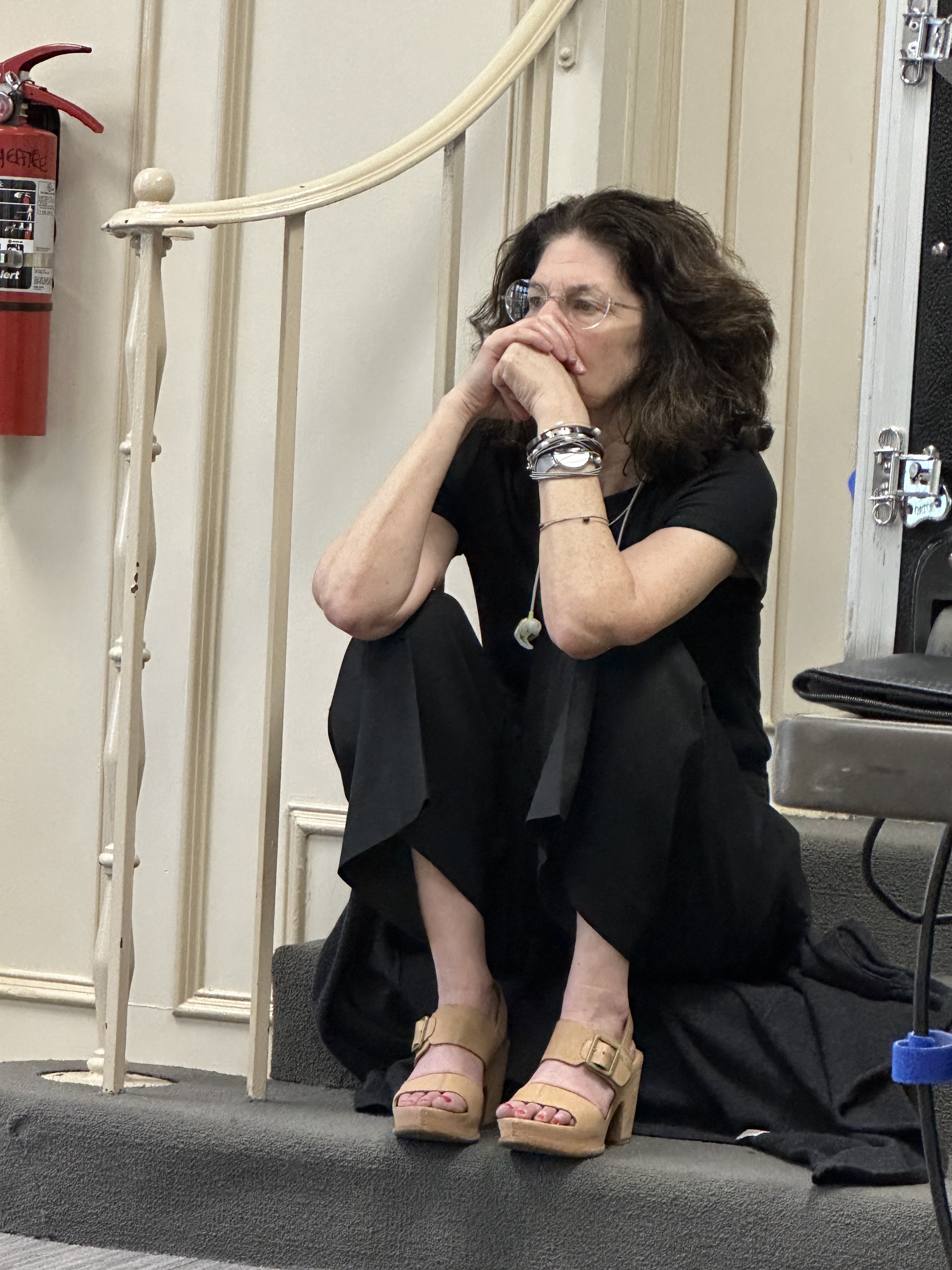 Woman seated on a stair, hands folded under her chin.