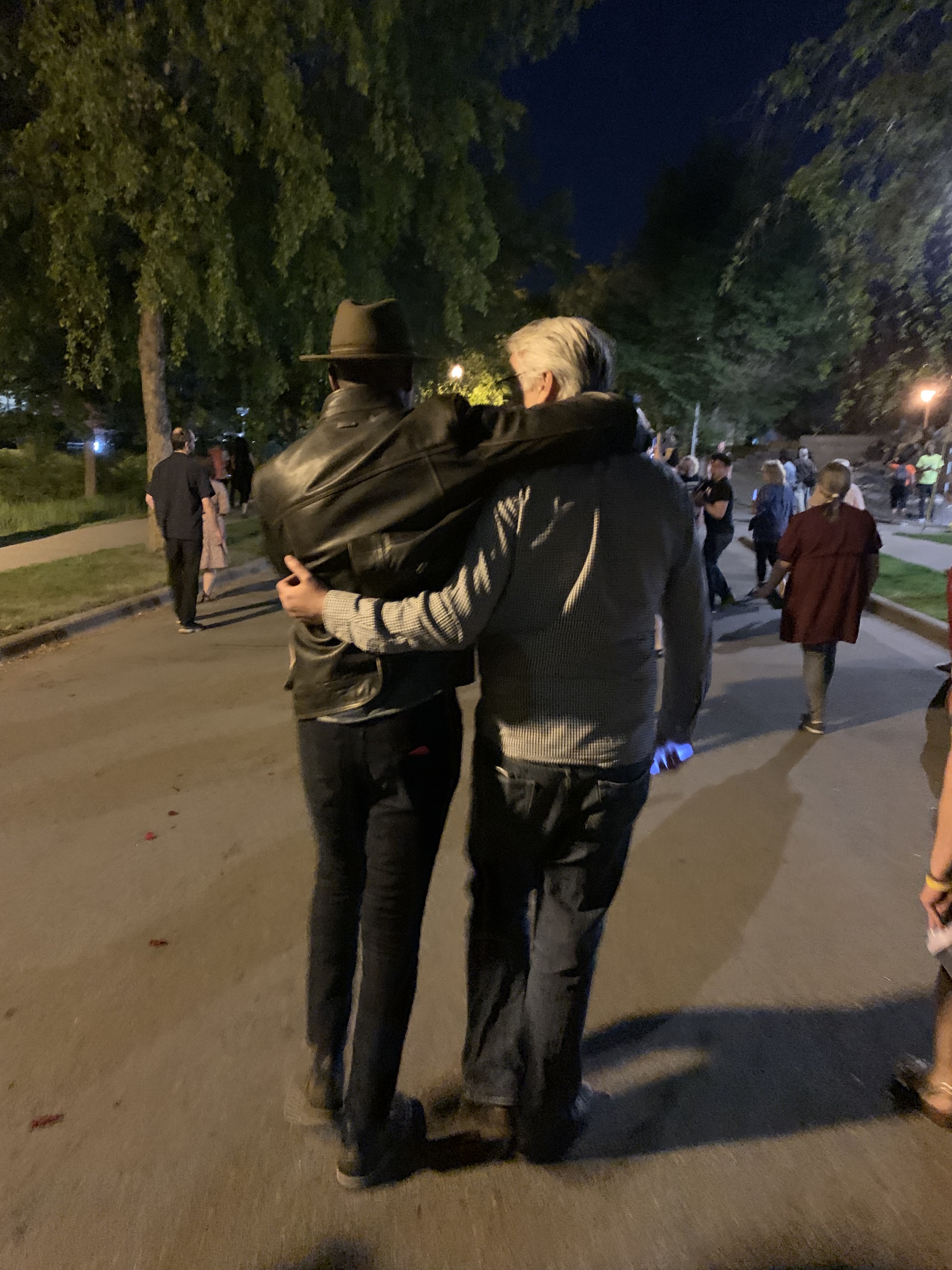 Two men walk, arms around one another.