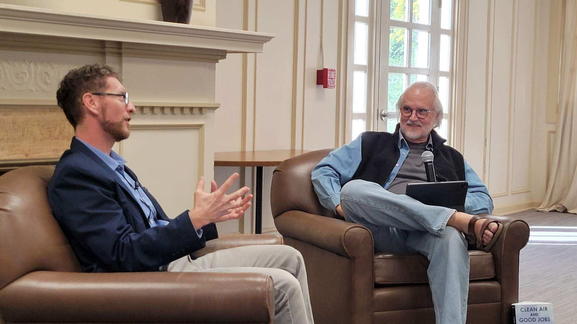two men sit in leather chairs, conversing and gesticulating