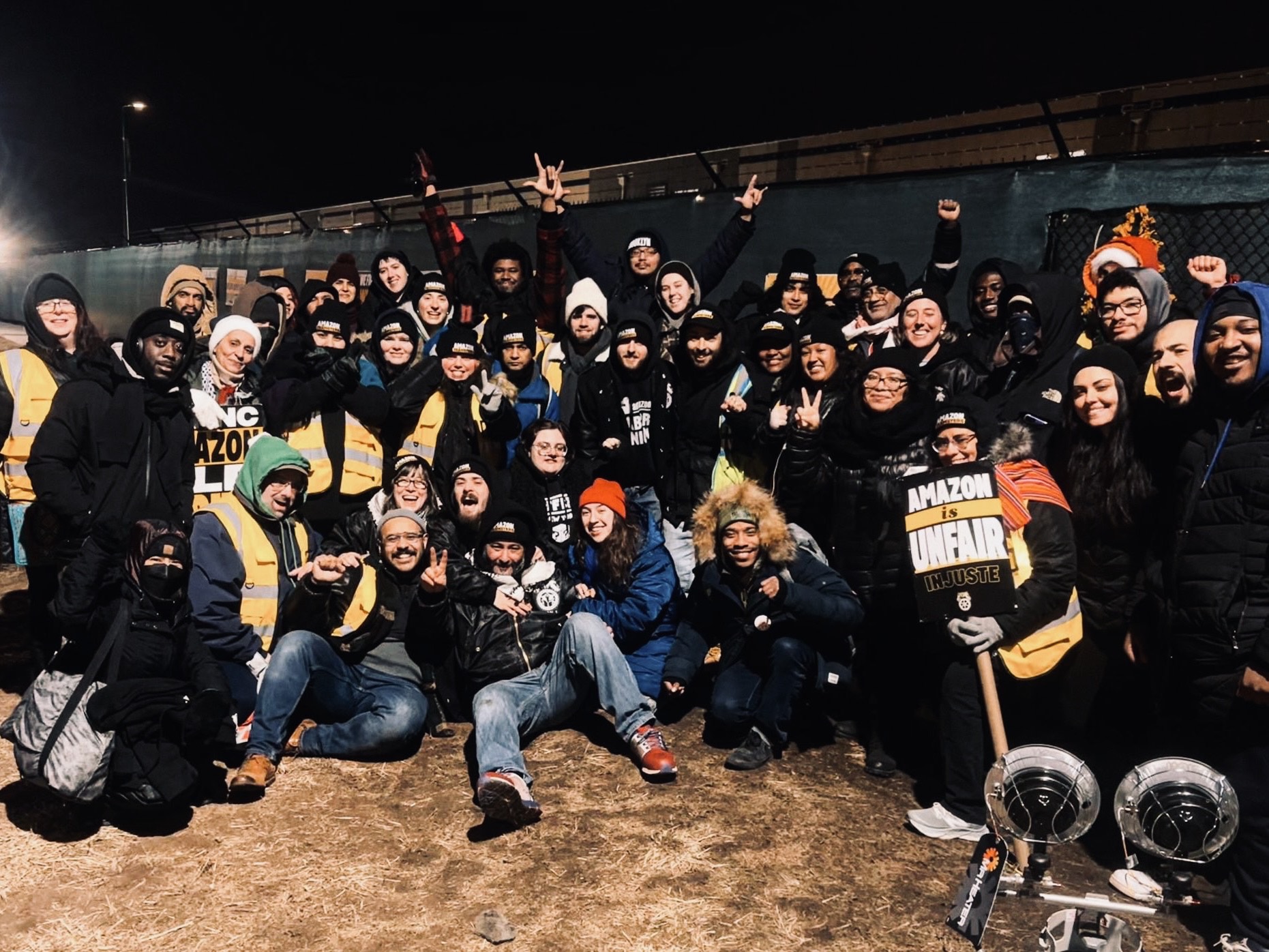 Large group of workers pose outside in hats and sweatshirts