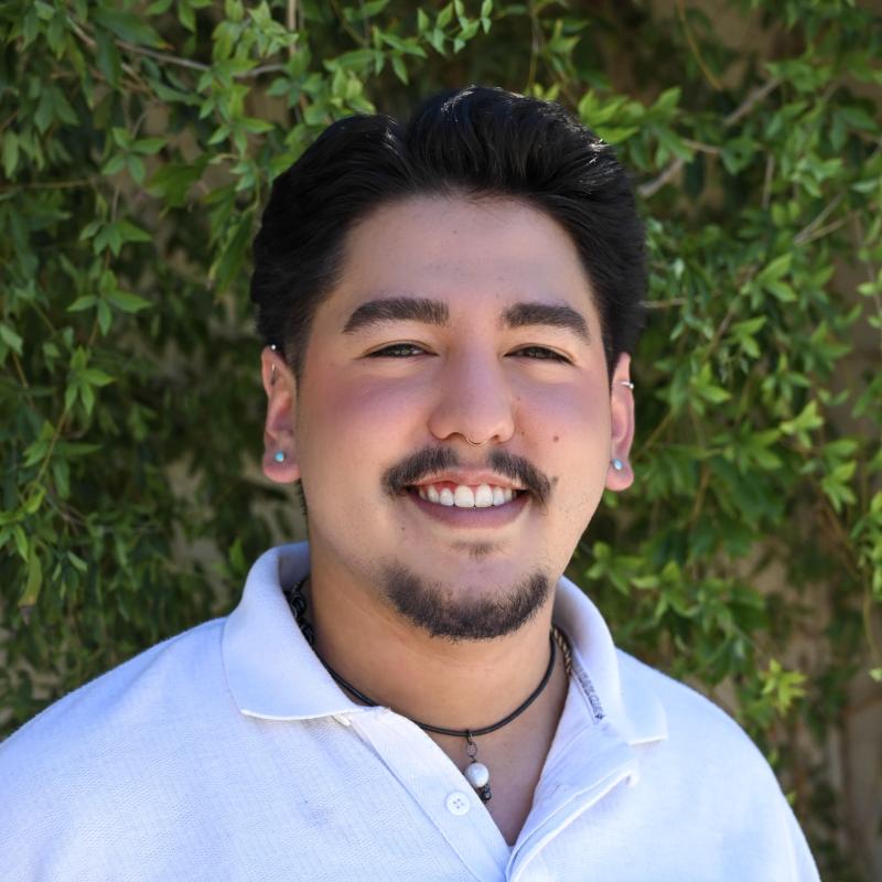 Young man in white shirt smiling in front of green background.